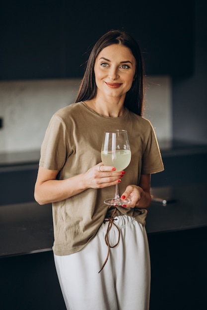 Mulher jovem bebendo limonada de vidro na cozinha