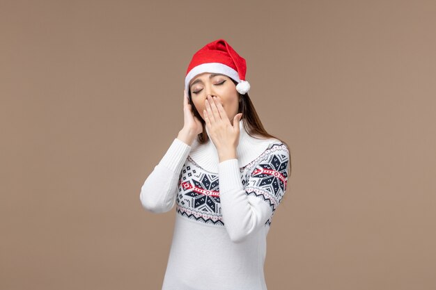 Mulher jovem bocejando com tampa vermelha sobre fundo marrom emoção de Natal ano novo