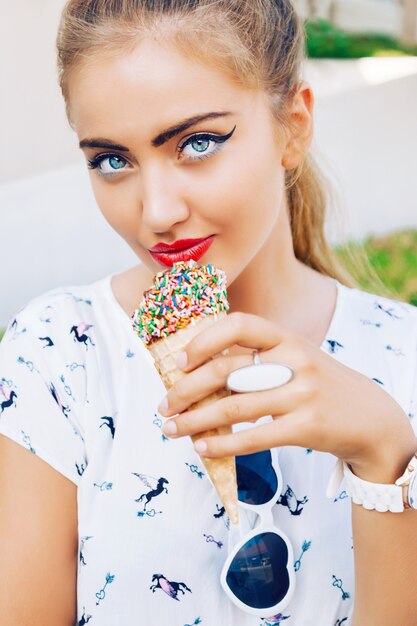 Mulher jovem bonita brincalhão feliz posando ao ar livre no horário de verão com sorvete, rindo e se divertindo na rua, usando um vestido retrô.
