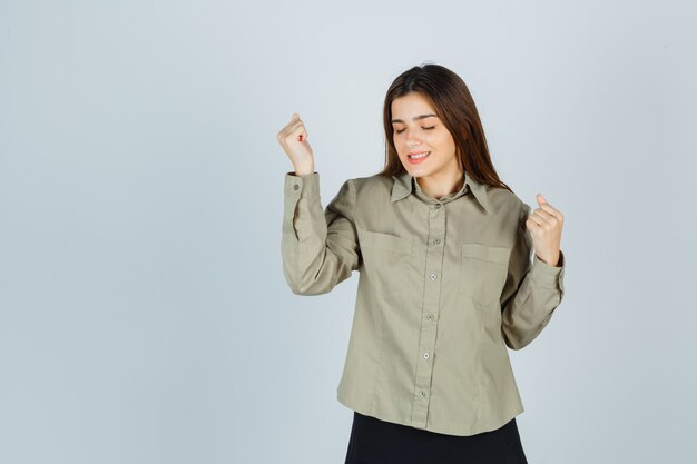 Mulher jovem bonita mostrando gesto de vencedor na camisa, saia e olhando feliz, vista frontal.