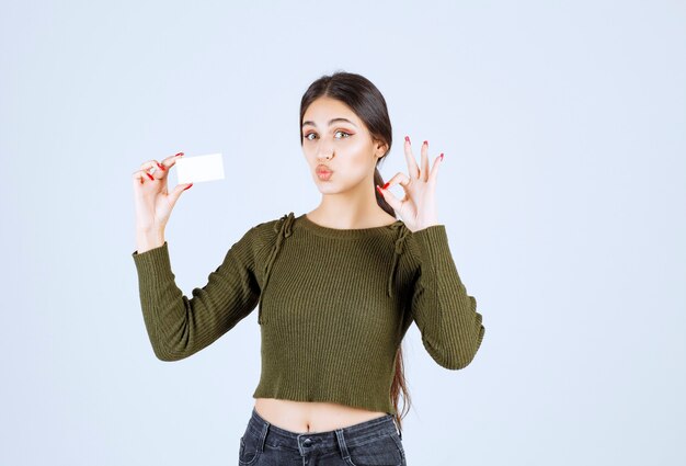 Mulher jovem bonita mostrando o cartão em branco e dando sinal de ok.