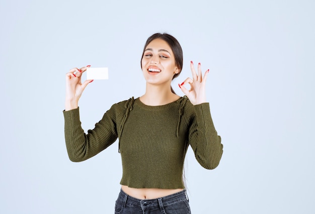 Mulher jovem bonita mostrando o cartão em branco e dando sinal de ok.