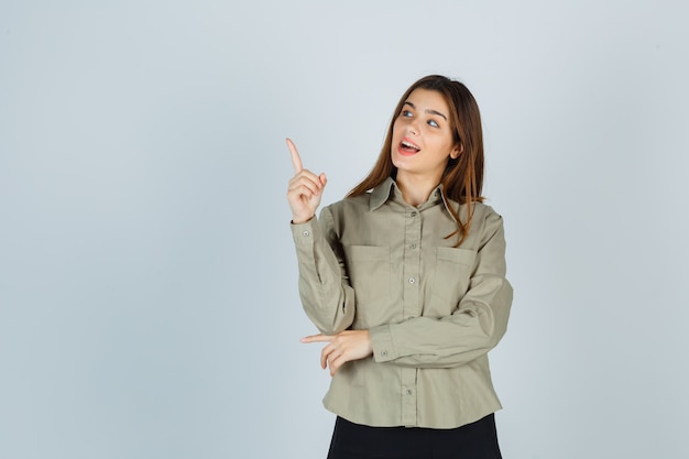 Mulher jovem bonita na camisa, saia apontando para cima e olhando maravilhada, vista frontal.