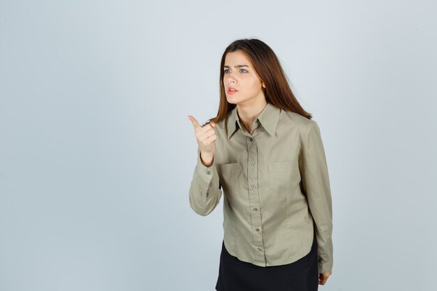 Mulher jovem bonita na camisa, saia aviso com o dedo e olhando furiosa, vista frontal.