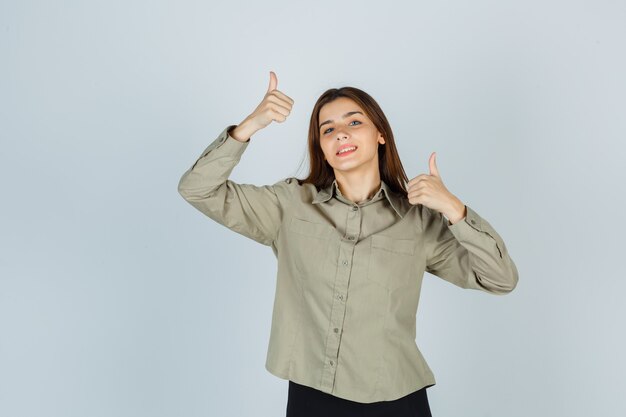 Mulher jovem bonita na camisa, saia mostrando dois polegares para cima e olhando feliz, vista frontal.