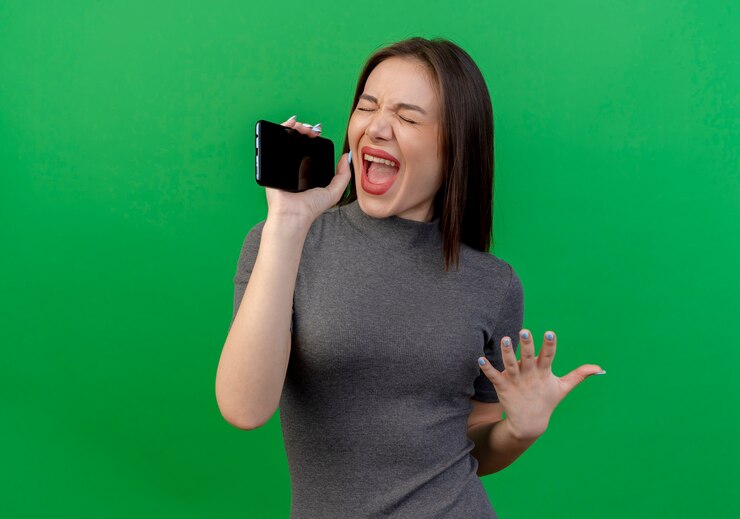 Foto grátis mulher jovem bonita segurando a mão no ar cantando com os olhos fechados, usando telefone celular como microfone