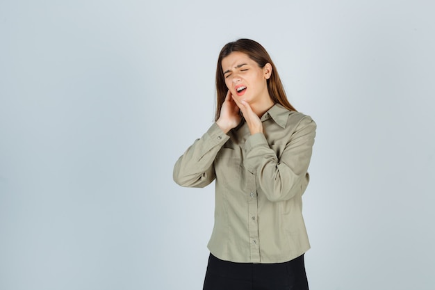 Mulher jovem bonita sofrendo de dor de dente na camisa, saia e parecendo dolorosa, vista frontal.