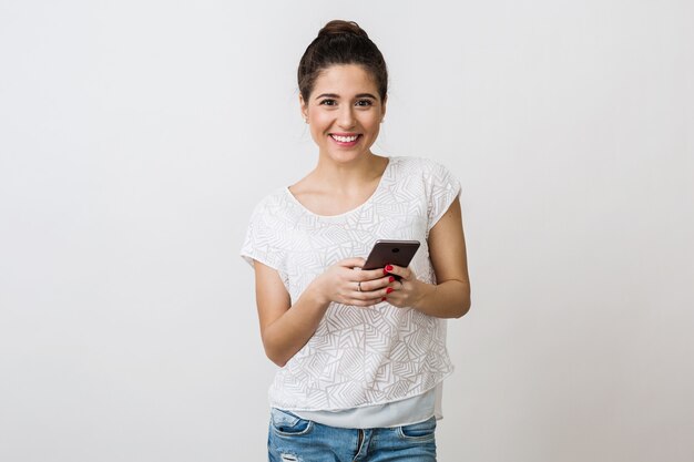 Mulher jovem bonita sorrindo em camiseta branca, segurando e usando smartphone, dispositivo móvel, isolado