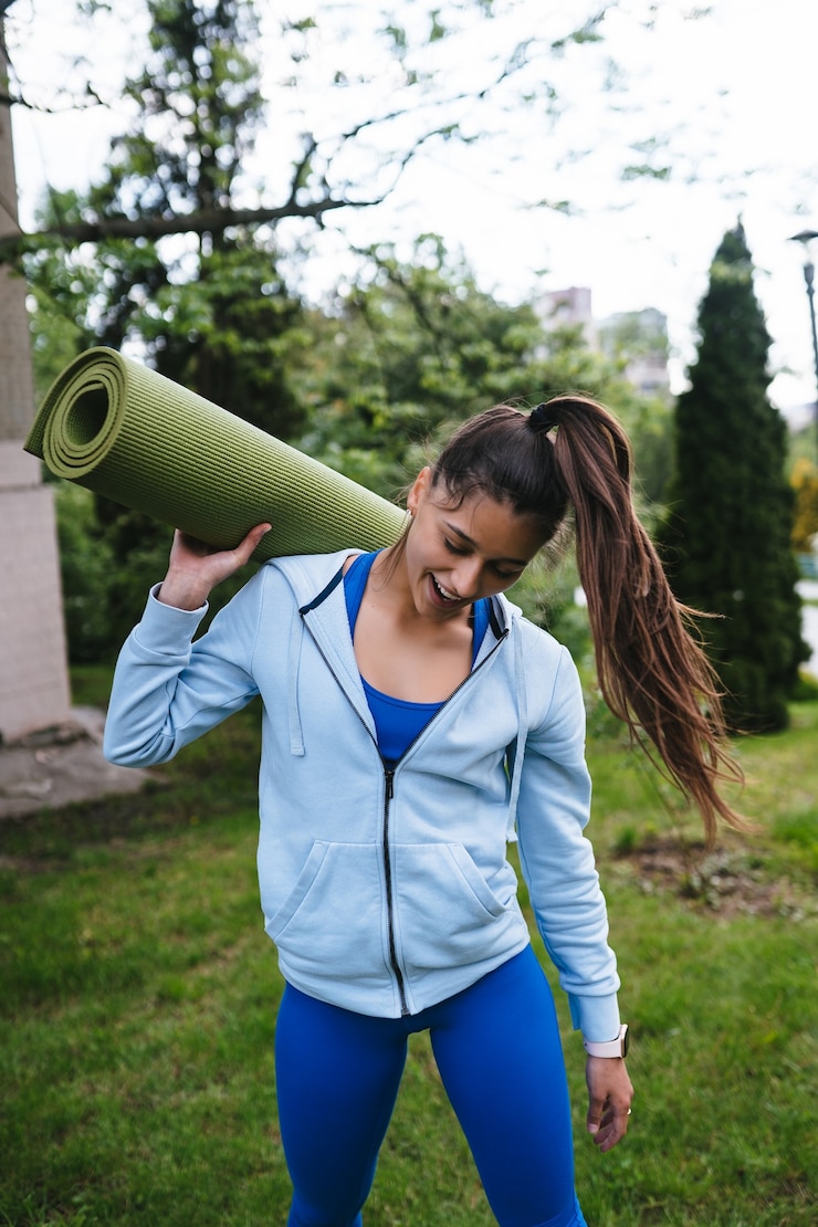 Foto grátis mulher jovem caminhando no parque urbano, segurando o tapete de fitness.
