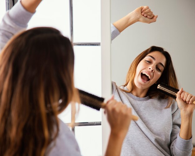 Mulher jovem cantando para a escova de cabelo em casa