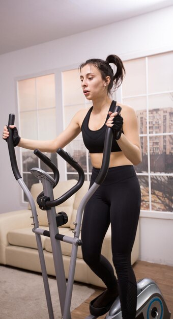 Mulher jovem caucasiana, fazendo um treino forte no elipsóide em casa.