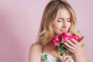 Foto grátis mulher jovem, cheirando, rosas, contra, fundo cor-de-rosa