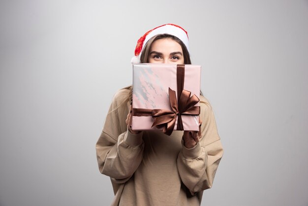 Mulher jovem cobrindo o rosto com um presente de Natal.