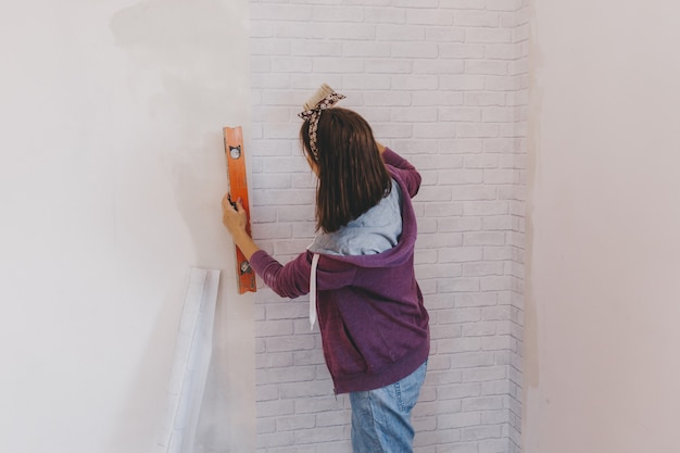Mulher jovem cola papel de parede em casa. garota cola papel de parede na forma de um tijolo. reparar.