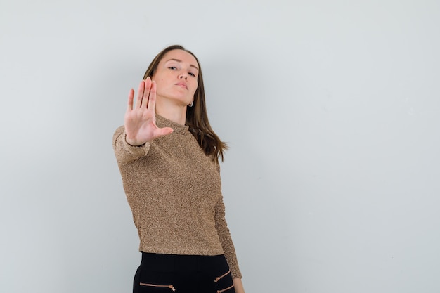 Mulher jovem com blusa dourada, mostrando um gesto de parar e parecendo severa