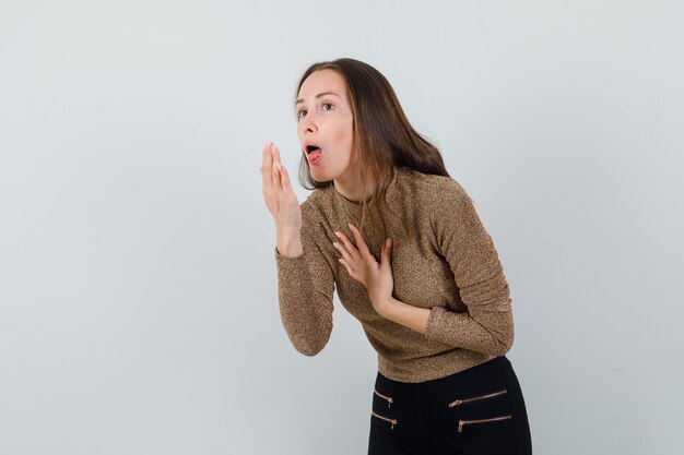 Mulher jovem com blusa dourada tossindo e parecendo preocupada