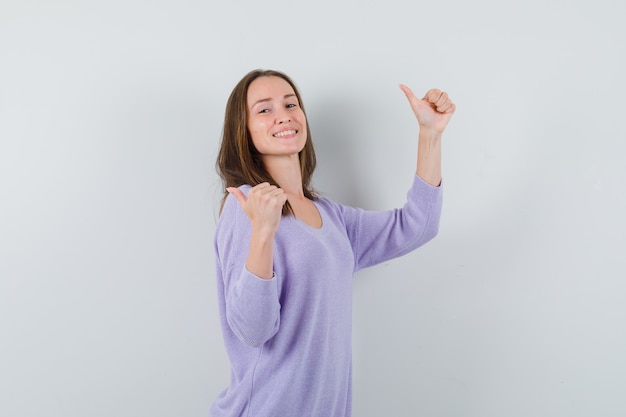 Mulher jovem com blusa lilás aparecendo com o polegar e parecendo confiante