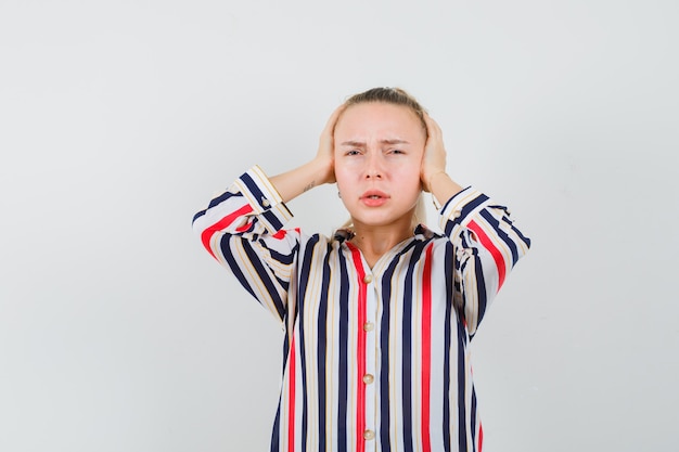 Mulher jovem com blusa listrada fechando as orelhas e parecendo exausta