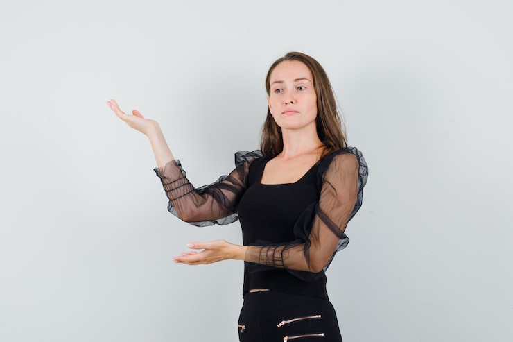 Foto grátis mulher jovem com blusa preta levantando as mãos com as palmas abertas de lado e olhando focado