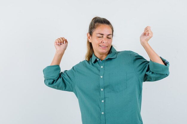 Mulher jovem com blusa verde mostrando o gesto do vencedor enquanto pisca e fica bonita