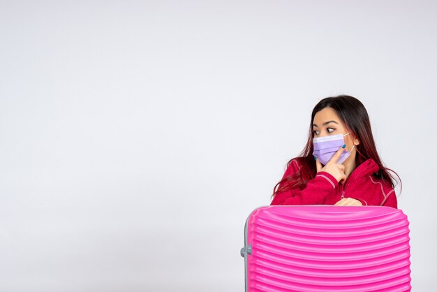 Mulher jovem com bolsa rosa na máscara na parede branca, mulher com vírus pandêmico, férias em cor branca, vista frontal