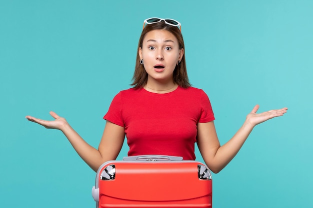 Mulher jovem com bolsa vermelha se preparando para as férias na mesa azul