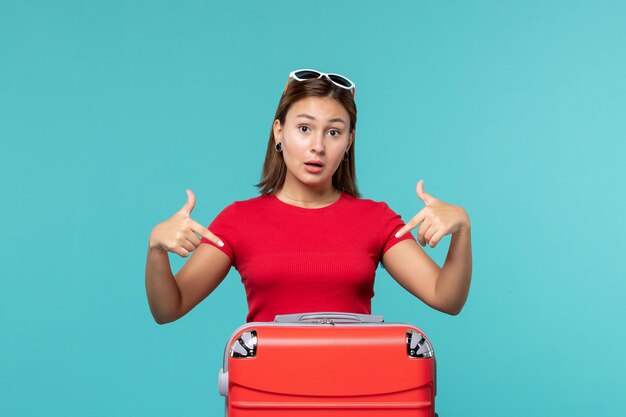 Mulher jovem com bolsa vermelha se preparando para as férias no espaço azul claro de frente