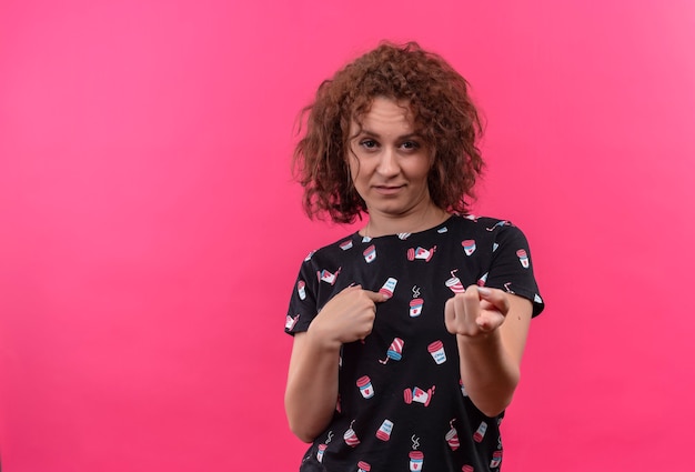 Mulher jovem com cabelo curto e encaracolado com expressão cética a apontar os dedos para si mesma e para a frente