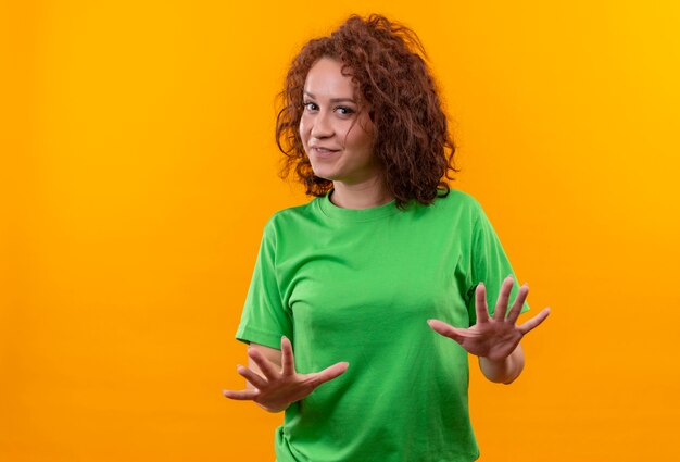 Foto grátis mulher jovem com cabelo curto e encaracolado em uma camiseta verde com as mãos estendidas dizendo não se aproxime de pé