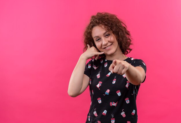 Mulher jovem com cabelo curto e encaracolado fazendo gesto de me chamar e apontando com o dedo na frente