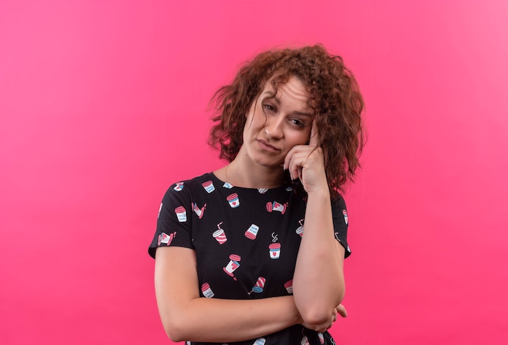 Foto grátis mulher jovem com cabelo curto e encaracolado parecendo cansada e entediada em pé sobre uma parede rosa