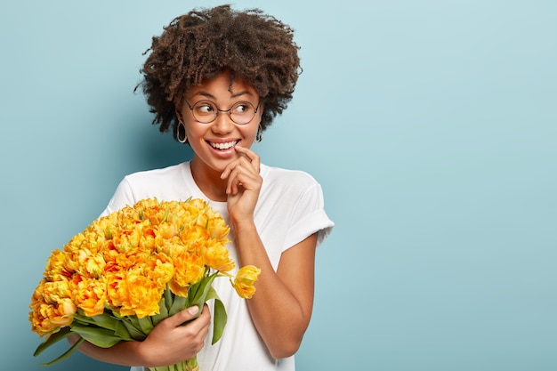 Foto grátis mulher jovem com cabelo encaracolado segurando um buquê de flores amarelas