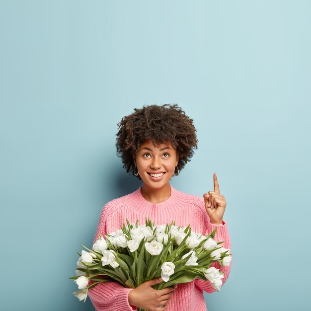 Mulher jovem com cabelo encaracolado segurando um buquê de flores brancas