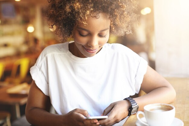 Mulher jovem com cabelo encaracolado sentada num café, a usar o telefone