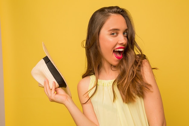 Mulher jovem com cabelo ondulado expressando emoções positivas em uma parede amarela