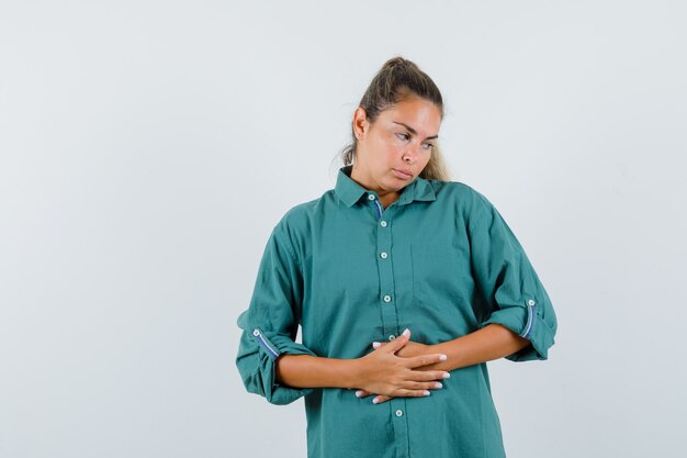 Mulher jovem com camisa azul segurando as mãos na barriga e parecendo entediante