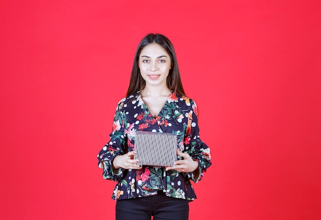 Mulher jovem com camisa floral segurando uma caixa de presente de prata