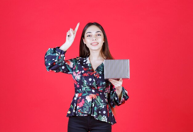 Mulher jovem com camisa floral segurando uma caixa de presente prateada e tem uma boa ideia