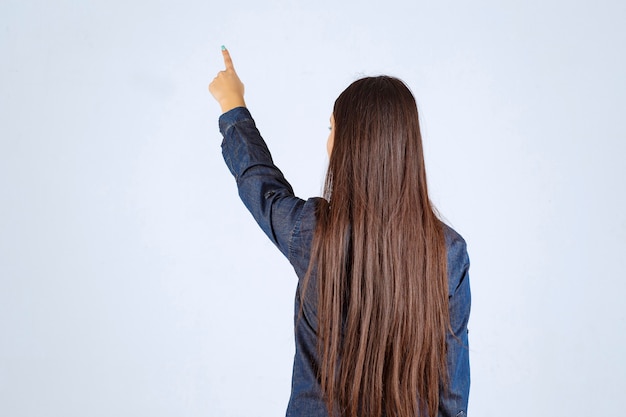 Mulher jovem com camisa jeans apontando para algo atrás