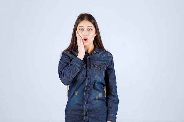 Mulher jovem com camisa jeans parece surpresa e animada