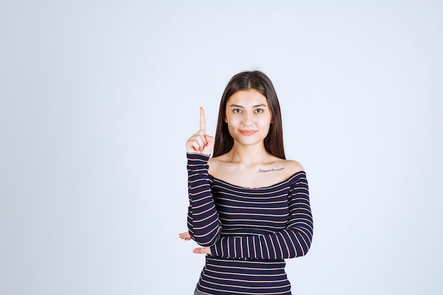 Mulher jovem com camisa listrada apontando para algo atrás