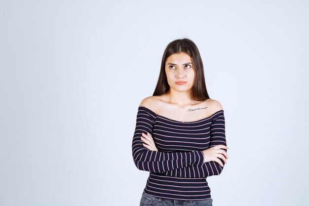 Mulher jovem com camisa listrada cruzando os braços e olhando séria