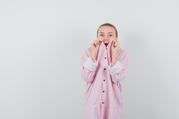 Mulher jovem com camisa rosa se escondendo atrás da gola e parecendo assustada