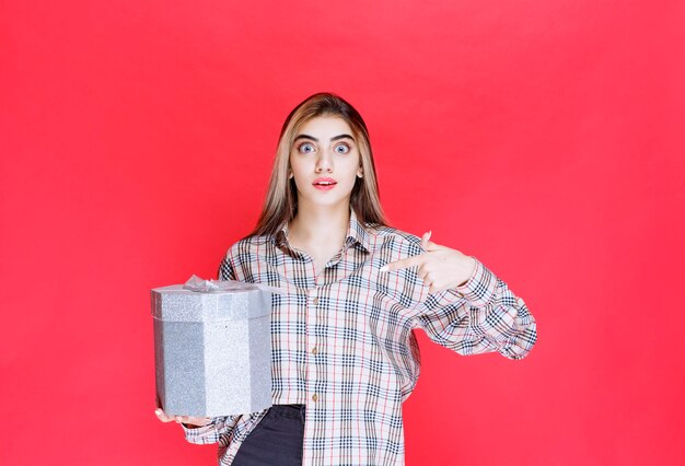 Mulher jovem com camisa xadrez segurando uma caixa de presente prateada