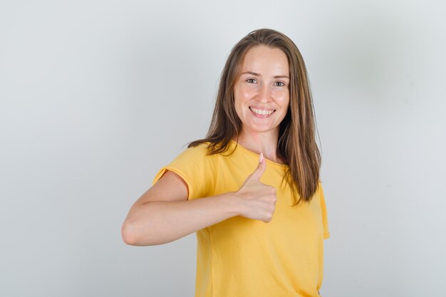 Mulher jovem com camiseta amarela mostrando o polegar e parecendo alegre