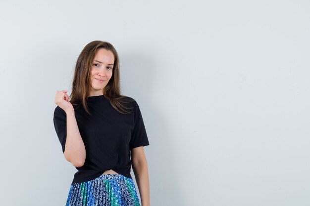 Foto grátis mulher jovem com camiseta preta e saia azul levantando um braço e sorrindo e parecendo feliz