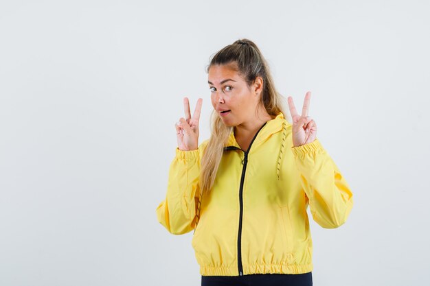 Mulher jovem com capa de chuva amarela mostrando o sinal em v