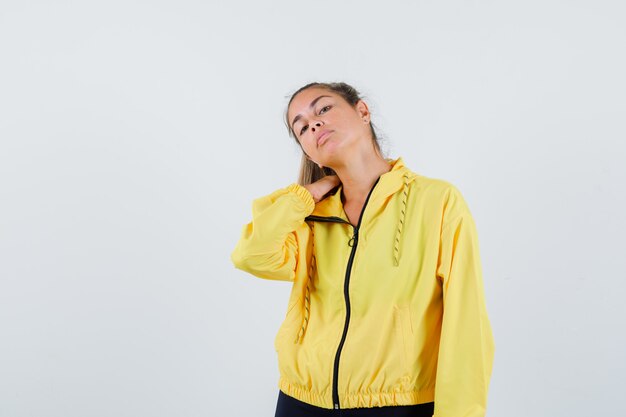 Mulher jovem com capa de chuva amarela, sofrendo de dor no pescoço e parecendo preocupada