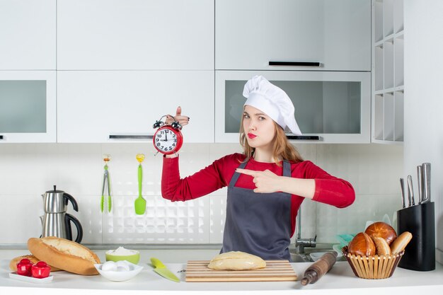 Mulher jovem com chapéu de cozinheira segurando um despertador vermelho de frente