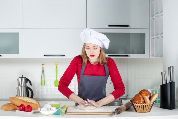 Mulher jovem com chapéu e avental de cozinheira amassando massa na cozinha